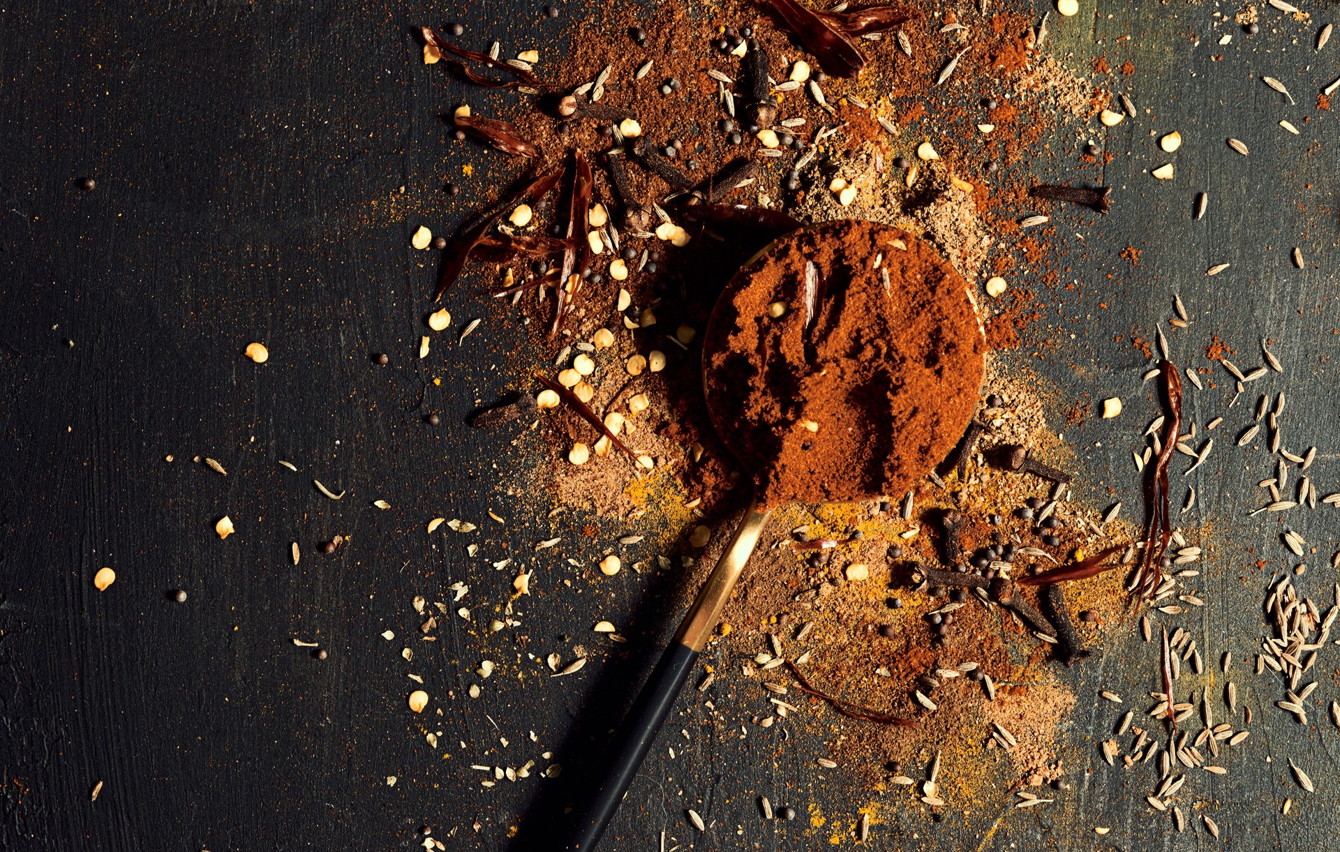 Spices, flavors and seasoning on a black wooden table in a kitchen, scattered with copy space. Above view of an assortment of Indian condiments for preparing a tasty and spicy meal at a restaurant